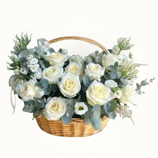 Floral arrangement with white roses and greenery in a woven basket on a white background
