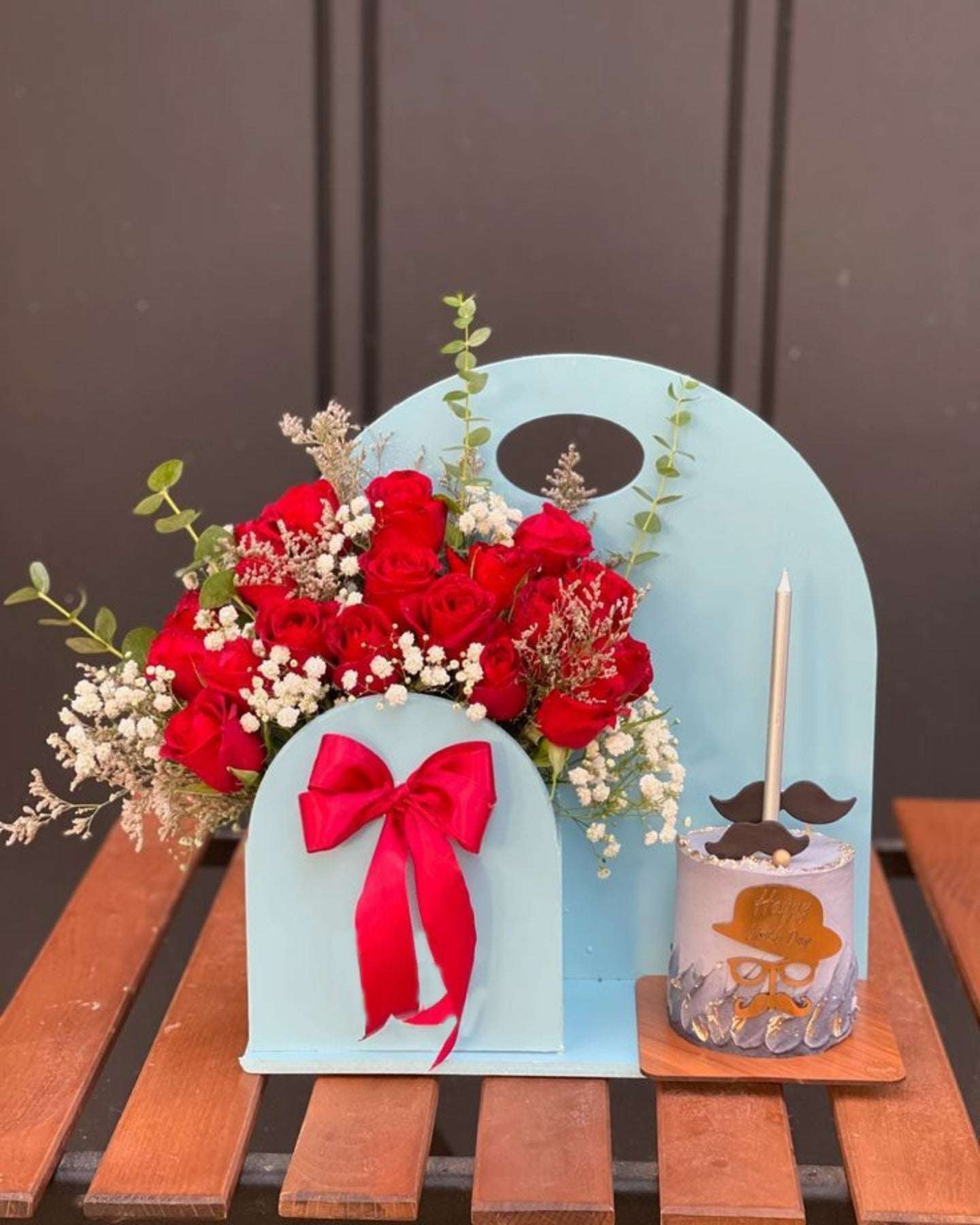 Decorative mailbox with red roses, a pink bow, and a small glass container on a wooden surface.
